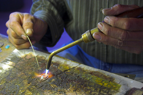 Hands of the craftsman-jeweler holding torch while making a piece of jewelry.